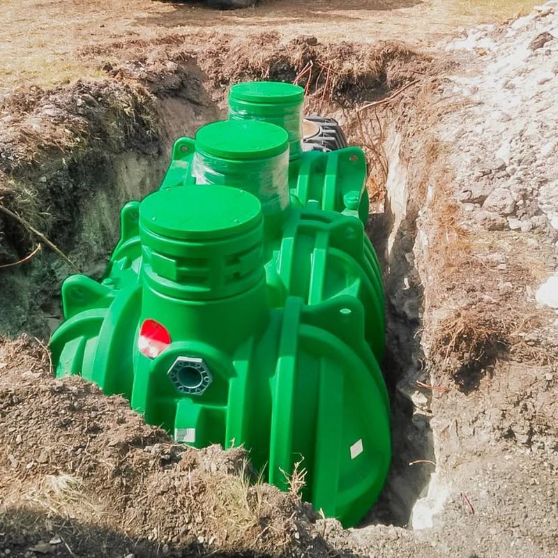 A new green septic tank set in the excavation before backfill.