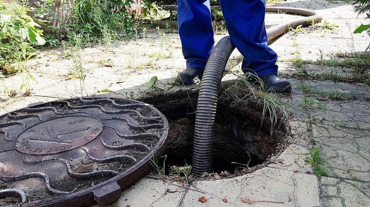 A technician working a suction hose into an open septic access during a pump-out.