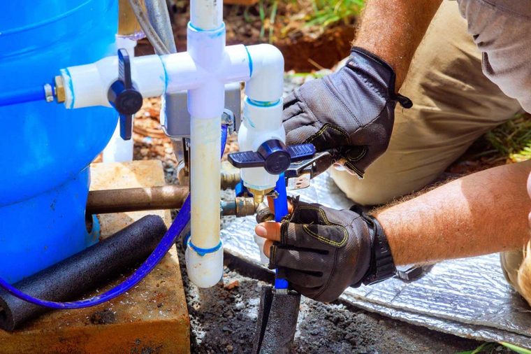 A technician fitting PVC pipework and valves on a well pressure system.